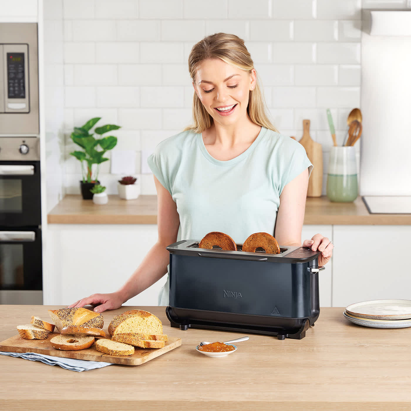 Eine Frau nutzt den Ninja Foodi Toaster im vertikalen Modus zum Toasten von zwei Bagel-Hälften in der Küche. Eine Frau nutzt den Ninja Foodi Toaster im vertikalen Modus zum Toasten von zwei Bagel-Hälften in der Küche.