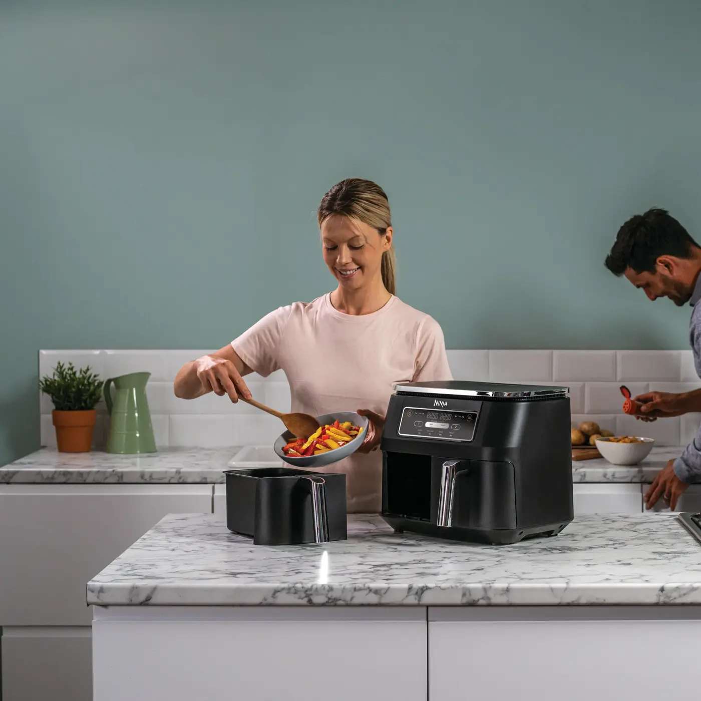 Person nimmt frisch zubereitetes Essen aus dem Dual-Zone Ninja Air Fryer. Person nimmt frisch zubereitetes Essen aus dem Dual-Zone Ninja Air Fryer.