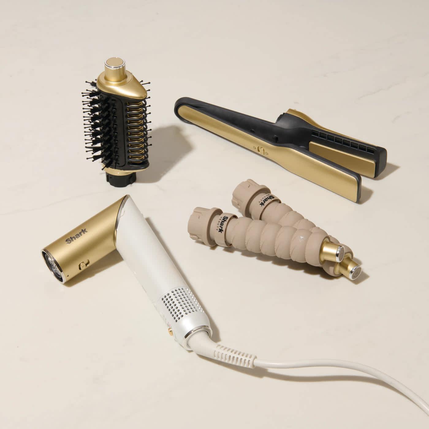 Produktset des Shark Glam Multistylers in Gold und Weiß mit Aufsätzen wie Silki-Glätteisen, Glossi-Warmluftbürste und Lockenaufsätzen.