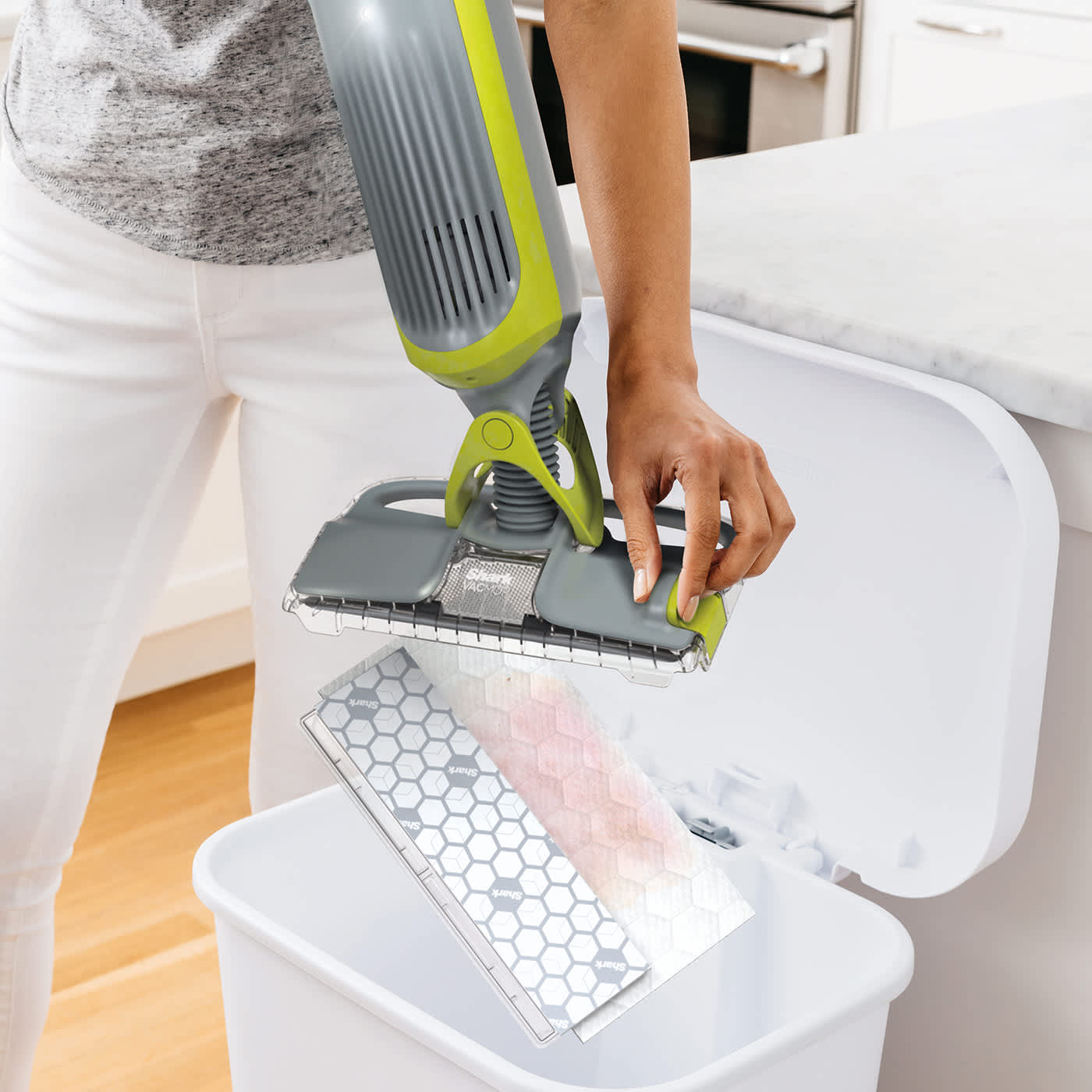 Hand hält Shark VM200EU mit entferntem schmutzigem Einwegpad über Mülleimer. Hand hält Shark VM200EU mit entferntem schmutzigem Einwegpad über Mülleimer.