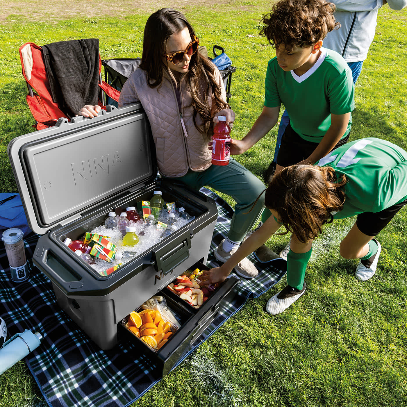 Mutter mit Kindern auf der Wiese, ein Kind nimmt Essen aus der Schublade der Ninja FrostVault Kühlbox