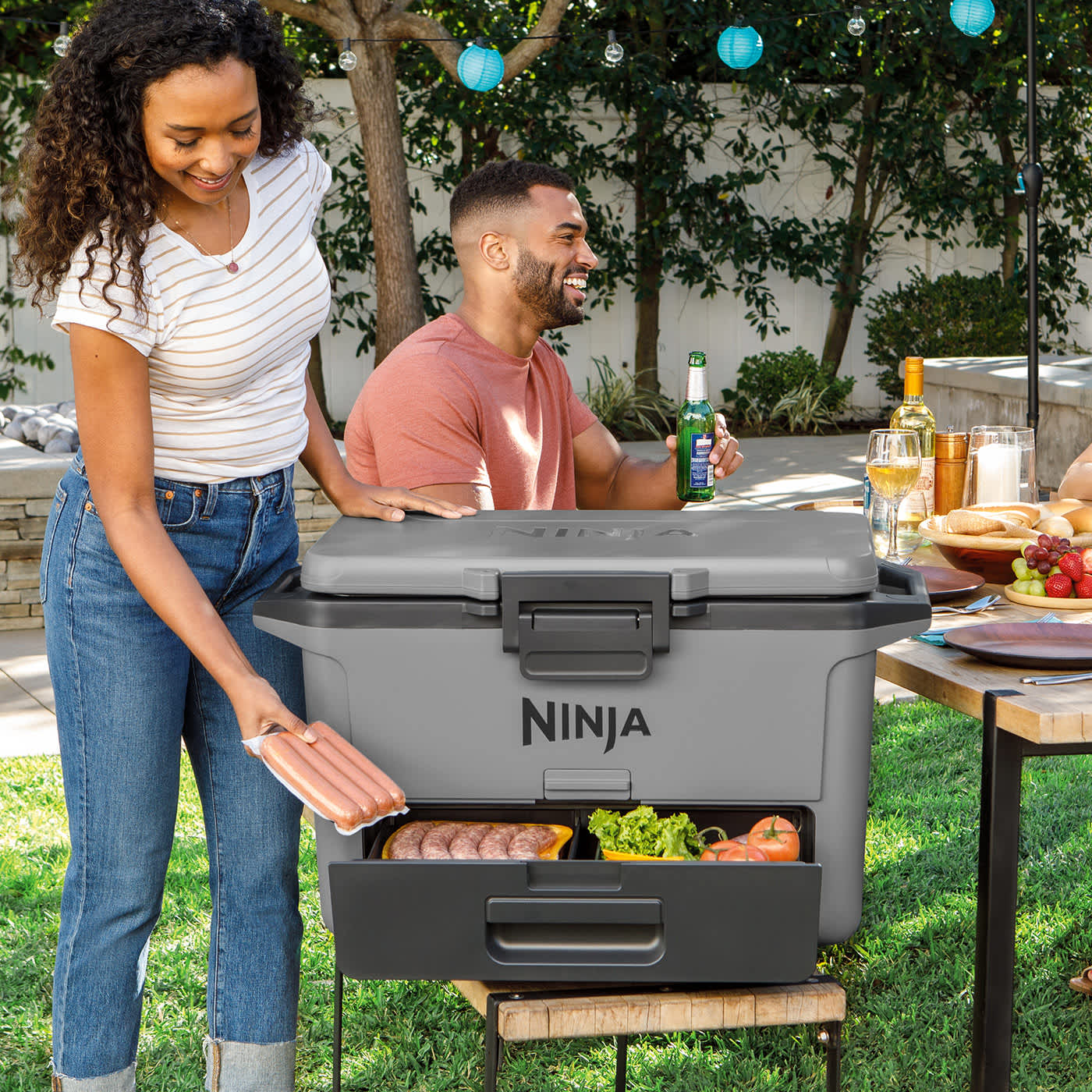 Person öffnet die Schublade der Ninja FrostVault Kühlbox mit Essen, Box steht auf einer Bank